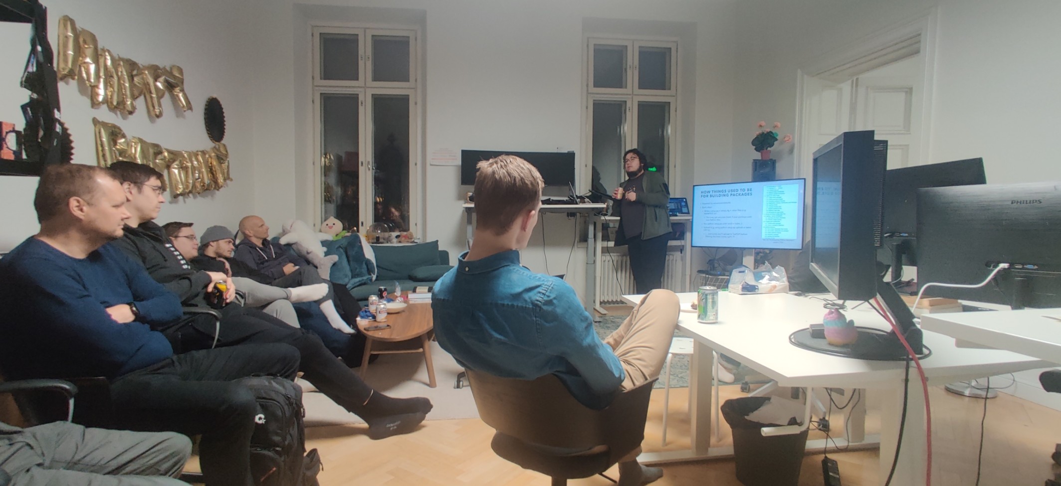 A group of developers sitting on a sofa and chairs in an office room with Aarni standing next to a screen, speaking to the audience.